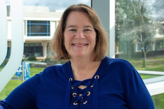 Edie Brown stands in the SSU student center, infront of a large windows. She's smiling and wearing a bright blue shirt.